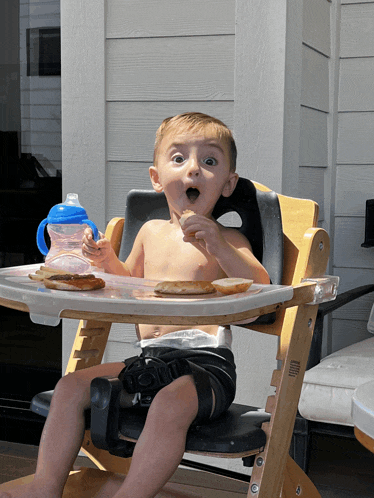 a young boy sitting in a high chair eating a sandwich
