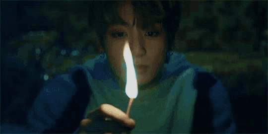 a young boy is holding a lit match in his hand in the dark .