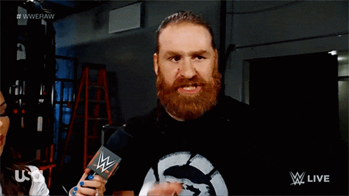 a bearded wrestler is pointing at something while holding a card that says ' wwe raw ' on it