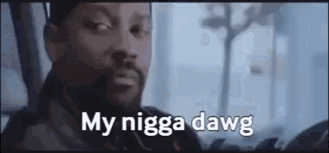 a man with a beard is sitting in a car with the words `` my nigga dawg '' written on the screen .