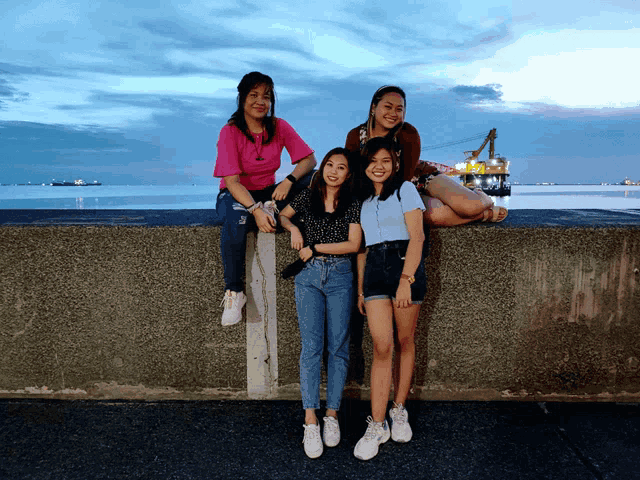 a group of young women pose for a picture on a concrete wall