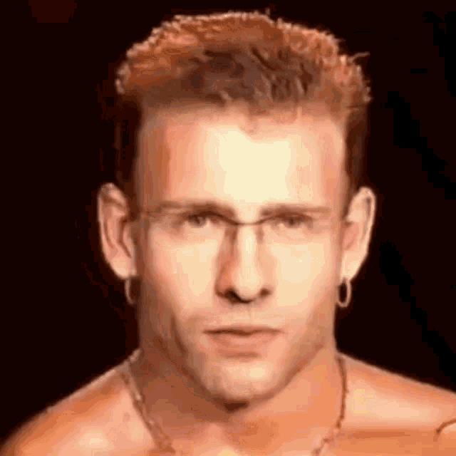a man wearing glasses and earrings is looking at the camera .