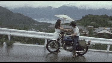 a woman holding an umbrella stands next to a man on a kawasaki motorcycle