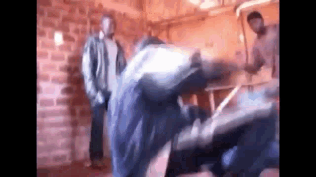 a blurry picture of two men standing next to each other in a room with a brick wall .
