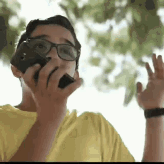 a young boy wearing glasses and a yellow shirt is talking on a cell phone .