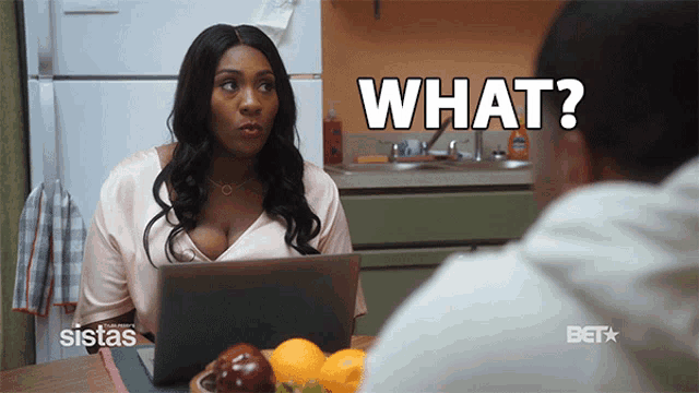 a woman sitting at a table with a laptop and a man asking what