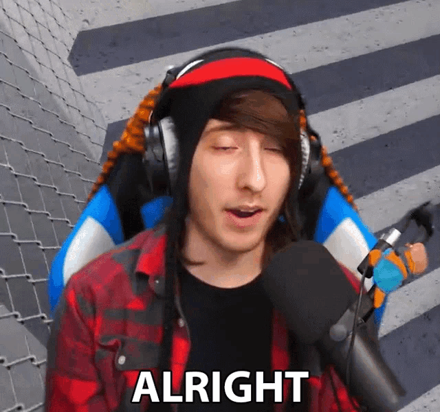 a man wearing headphones and a plaid shirt says " alright " in front of a microphone