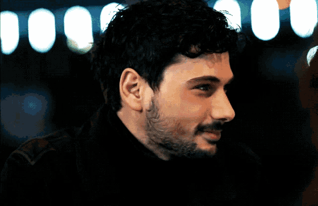 a man with a beard wearing a black turtleneck smiles for the camera