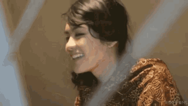 a woman is smiling and looking at the camera while standing in front of a mirror .