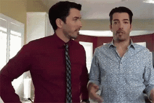 two men are standing next to each other in a kitchen talking to each other .
