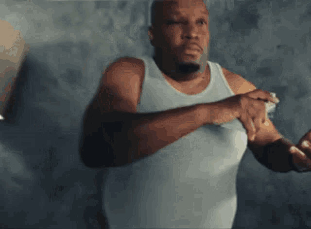 a man in a white tank top is making a gesture with his hands