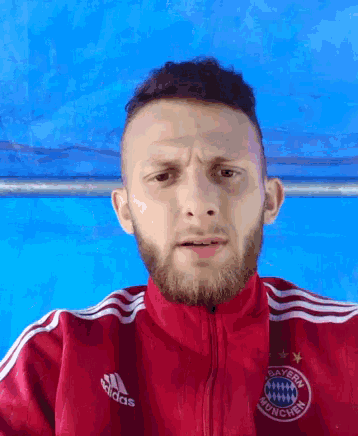 a man with a beard wears a red adidas jacket with the bayern munchen logo on it