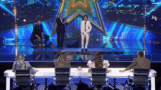 a man in a white suit stands on a stage in front of an audience