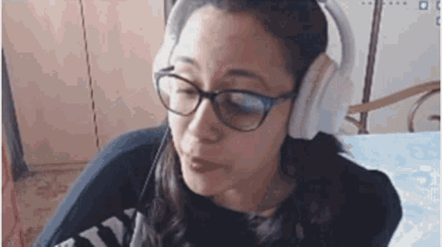 a woman wearing glasses and headphones is sitting on a bed and making a funny face .