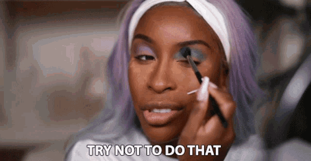 a woman with purple hair is applying makeup to her face while saying try not to do that .