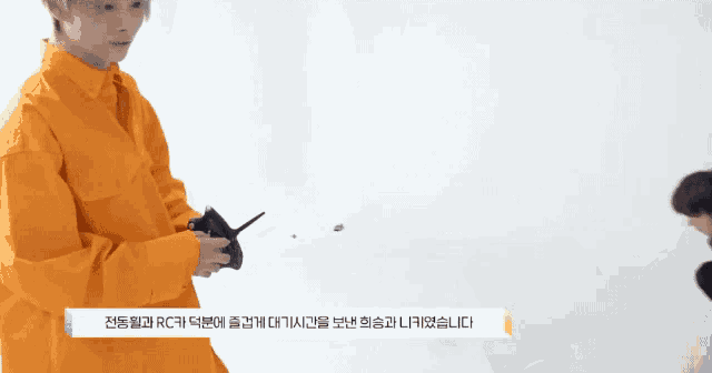 a man in an orange shirt is holding a remote control while another man looks on