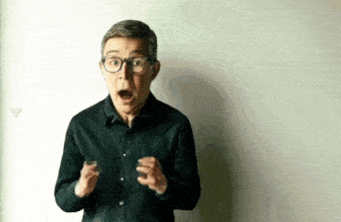 a man in a black shirt and glasses is making a surprised face .