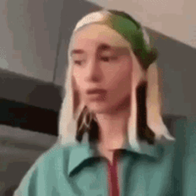 a woman with blonde hair and a green headband is wearing a green jacket and earrings .
