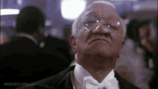 an older man in a tuxedo and bow tie is looking up at something .