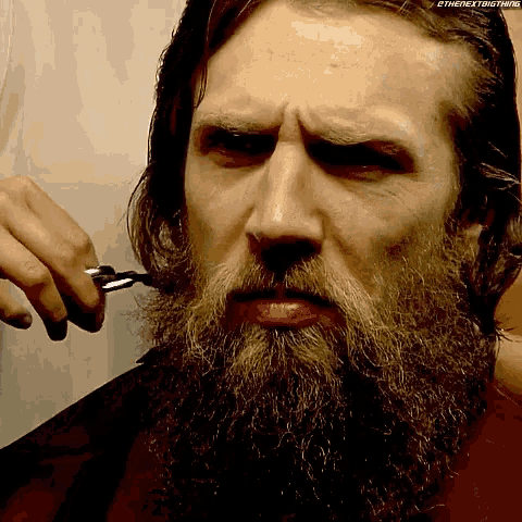 a man with a beard is getting his beard trimmed by someone