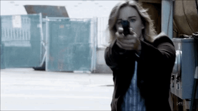 a woman holding a gun in front of a fence and a sign that says mb