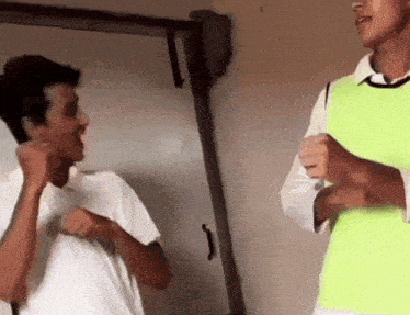 two young men are standing next to each other and one is wearing a green vest