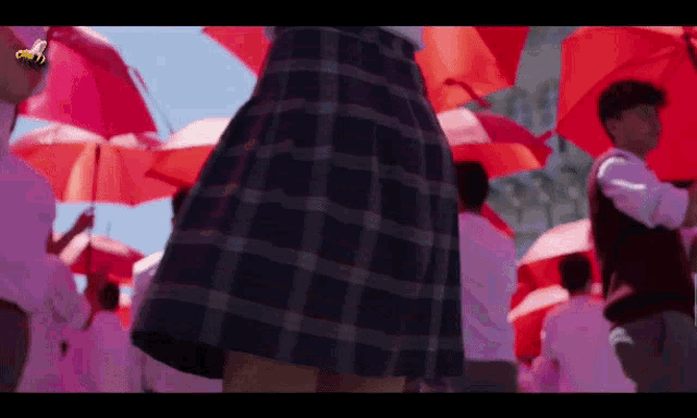 a woman in a plaid skirt stands in front of a crowd of people holding red umbrellas