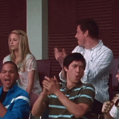 a group of people are sitting in a stadium clapping their hands