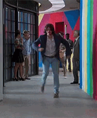a man in a blue jacket is running in a hallway with people standing around