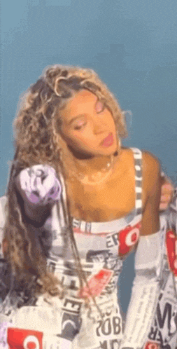 a woman with curly hair is standing in front of a blue background wearing a white and red dress .