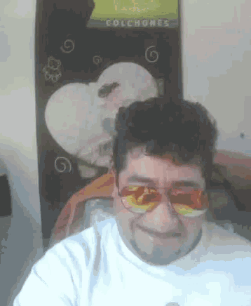 a man wearing sunglasses stands in front of a colchones poster