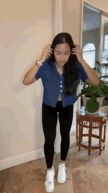 a woman in a blue shirt and black leggings is standing in a room