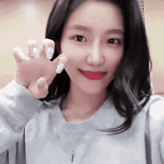 a woman with long black hair and white nails is smiling and waving at the camera