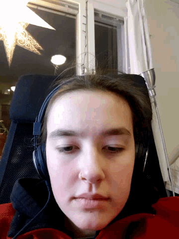 a woman wearing headphones looks at the camera in front of a window
