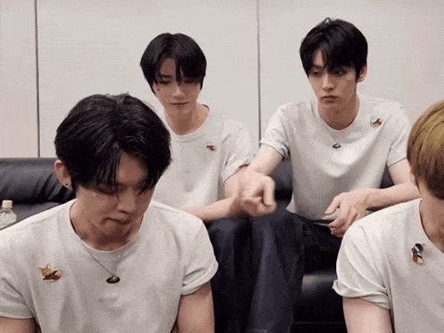 a group of young men are sitting on a couch and one of them has a necklace with a bird on it