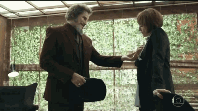 a man in a suit holds a woman 's hand in front of a window with blinds
