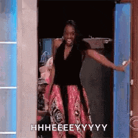 a woman in a dress is standing in a doorway with her arms outstretched and smiling .