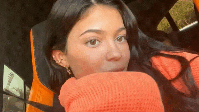 a close up of a woman wearing an orange sweater and earrings
