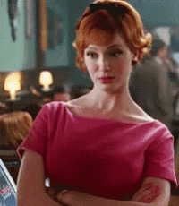 a woman in a pink dress with her arms crossed is standing in a room .