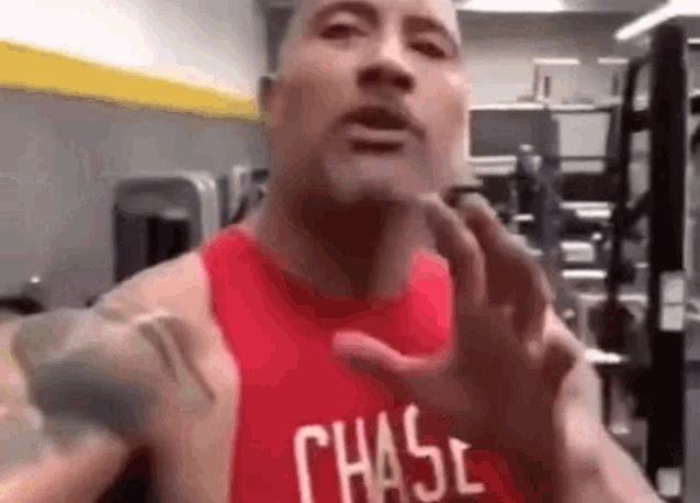 a man in a red tank top is standing in a gym and making a funny face .