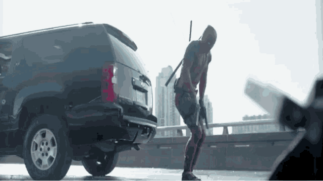 a man in a superhero costume is standing in front of a suv .