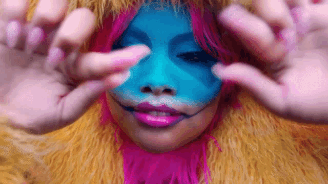 a woman with blue paint on her face is making a face with her hands
