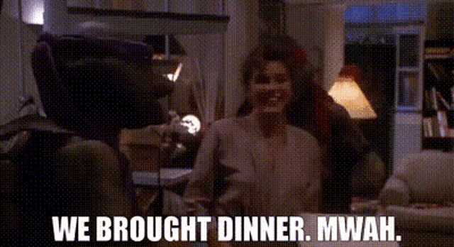 a woman is sitting at a table in a living room talking to a man and a robot .