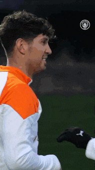 a soccer player wearing an orange and white jacket is standing on a field .