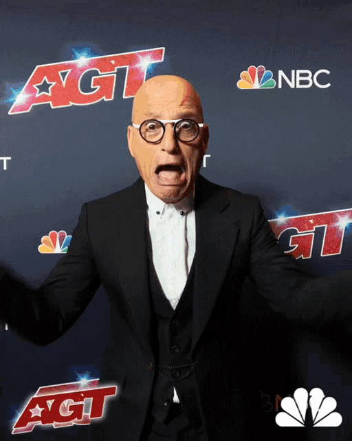 a bald man in a suit stands in front of a nbc sign