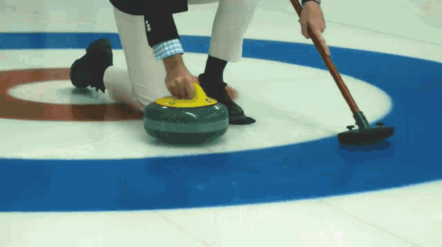 a person playing curling with a yellow stone that says ' a.s.a. ' on it
