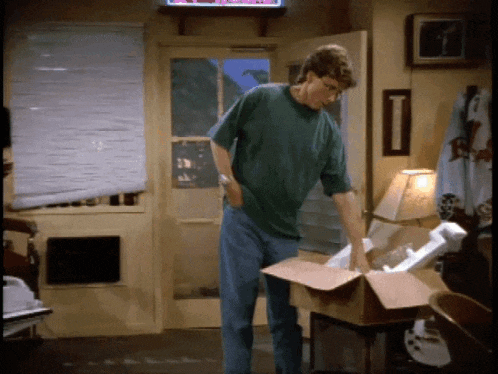 a man in a green shirt opens a cardboard box in a living room