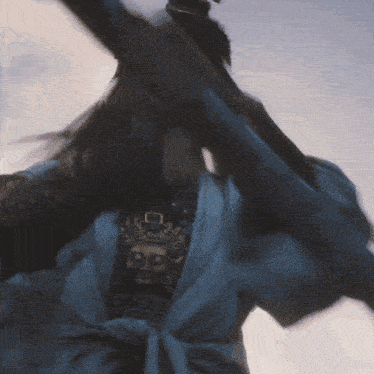 a person in a blue robe is holding a sword and a necklace with a buddha face on it