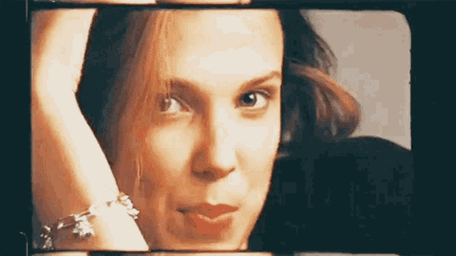 a close up of a woman 's face with a bracelet on her wrist looking at the camera .
