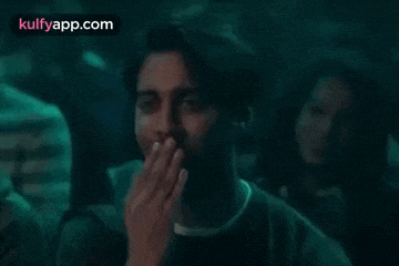 a man is covering his mouth with his hand in a dark room while watching a movie .